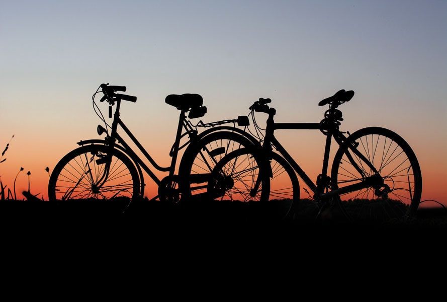 An image of two bike silhouettes on grass with the sun rise coming up.