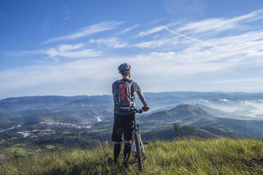 An image of a man stood with his bike looking across a hilly landscape.